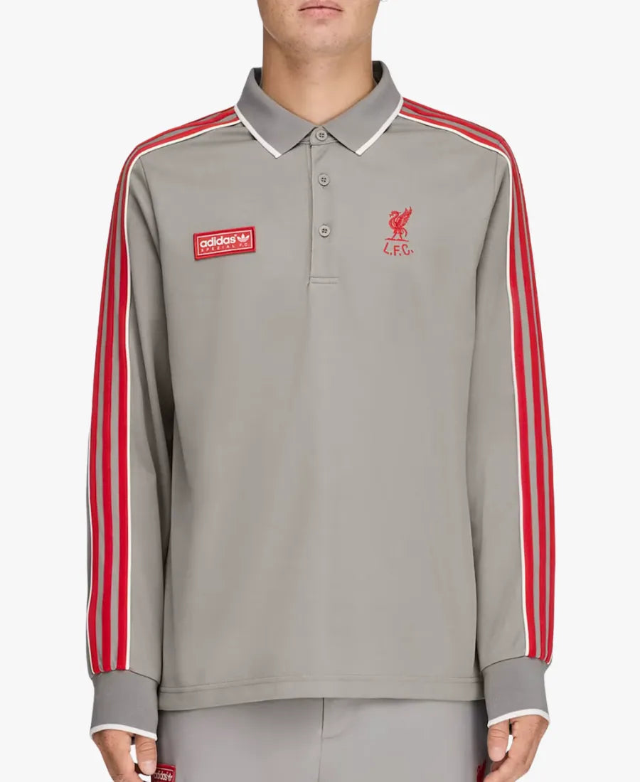 A man wearing a light gray long-sleeve polo shirt with red and white stripes down the sleeves, featuring a red Adidas logo patch on the right chest and a red Liverpool FC crest on the left chest.