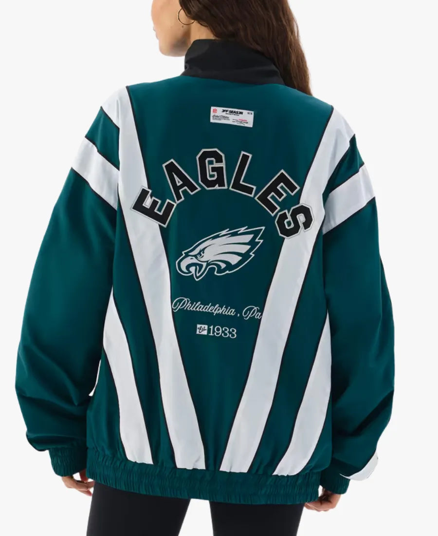 A woman shown from the back wearing a Philadelphia Eagles themed jacket. The jacket features dark teal green and white diagonal stripes with 'EAGLES' and the team logo printed on the back.